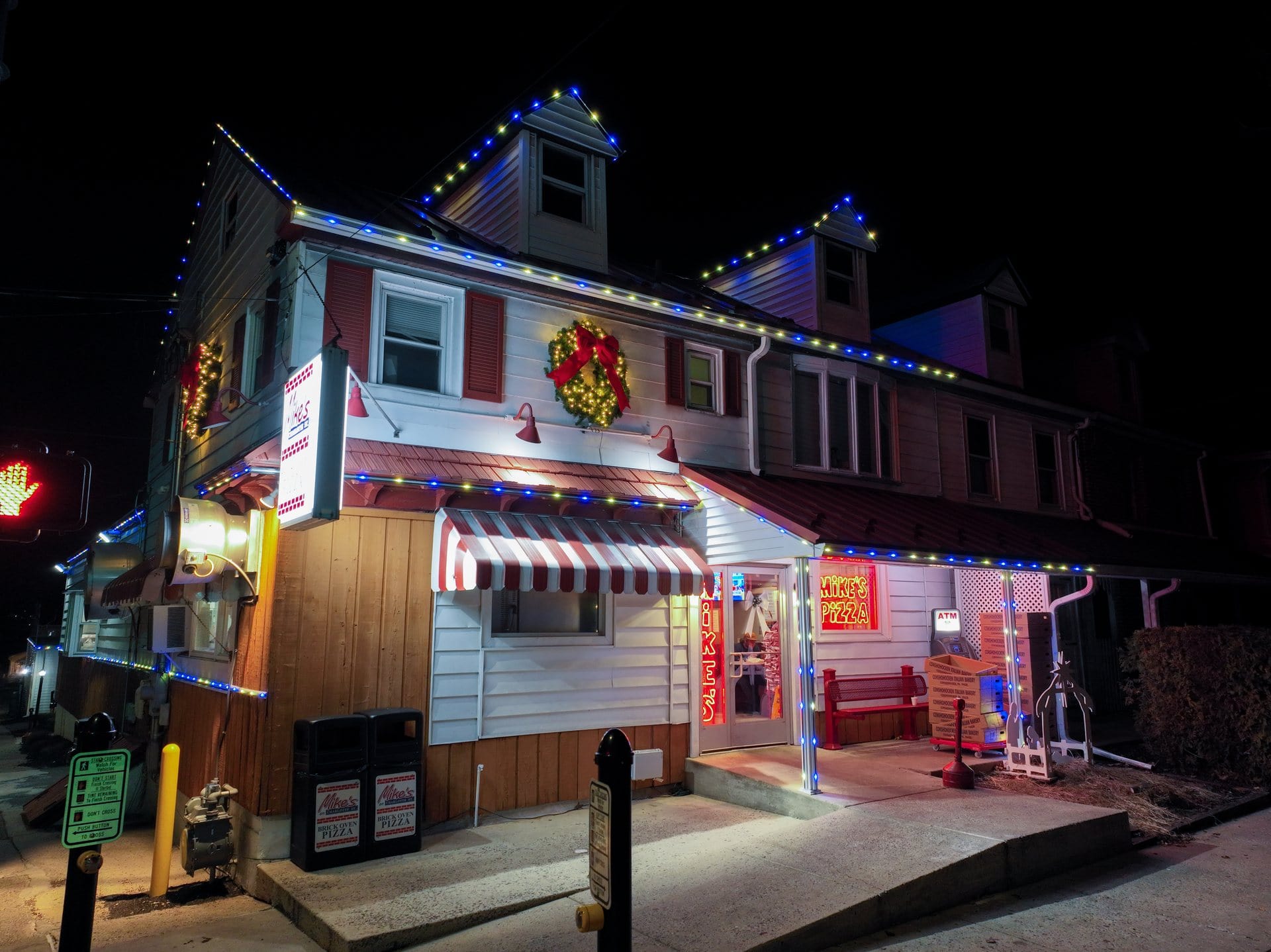 A diner with holiday lights and wreaths, glowing neon signs, and a striped awning at night.