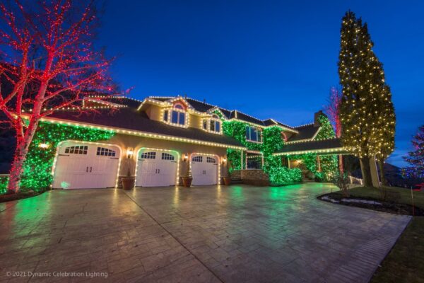 Large house decorated with white and green holiday lights at night, with trees also lit up.