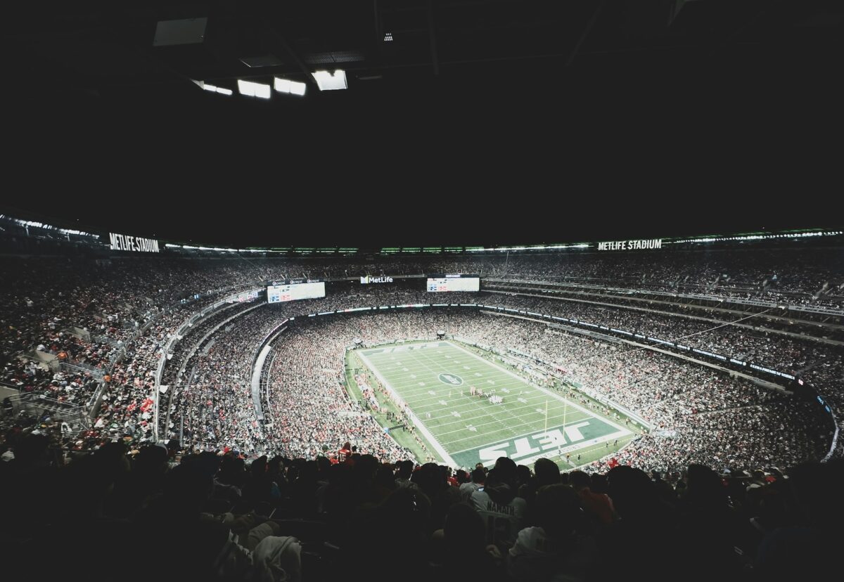 A packed football stadium at night with a game in progress on a brightly lit field.