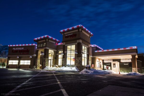 A modern car wash building at night, lit with red and white lights, snow piled around the parking lot.